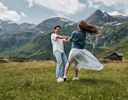 Summer in the mountains A man and woman dancing in a grassy field with mountains in the background.
