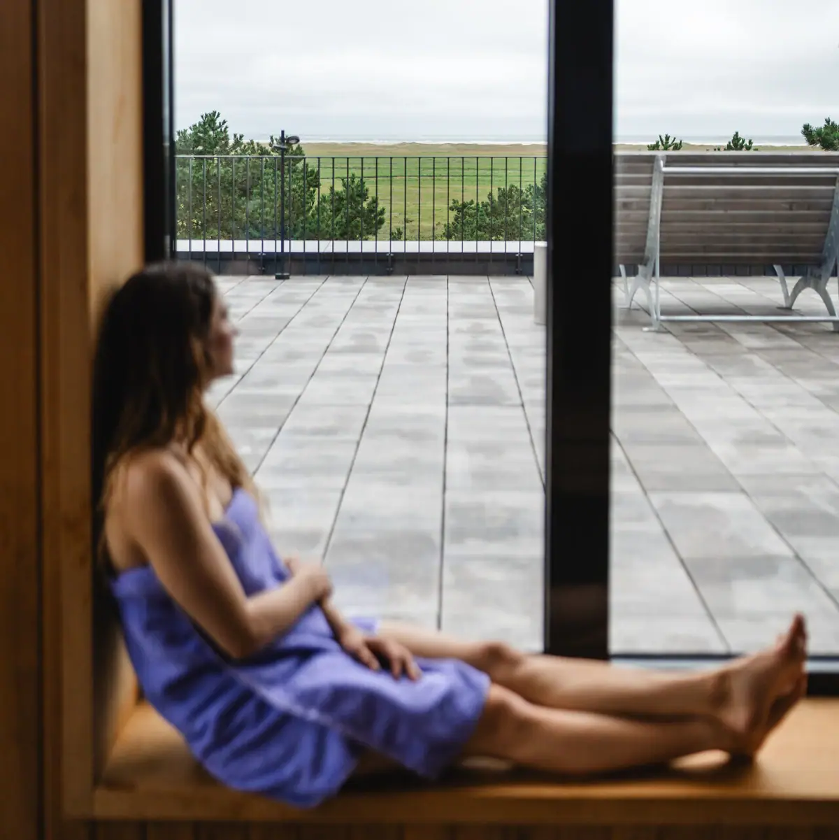 Sauna A woman is sitting on a windowsill in the sauna at the Urban Nature Hotel in St. Peter-Ording, looking out of the window.