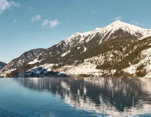 Mountains during winter A body of water with snow-covered mountains under a blue sky.