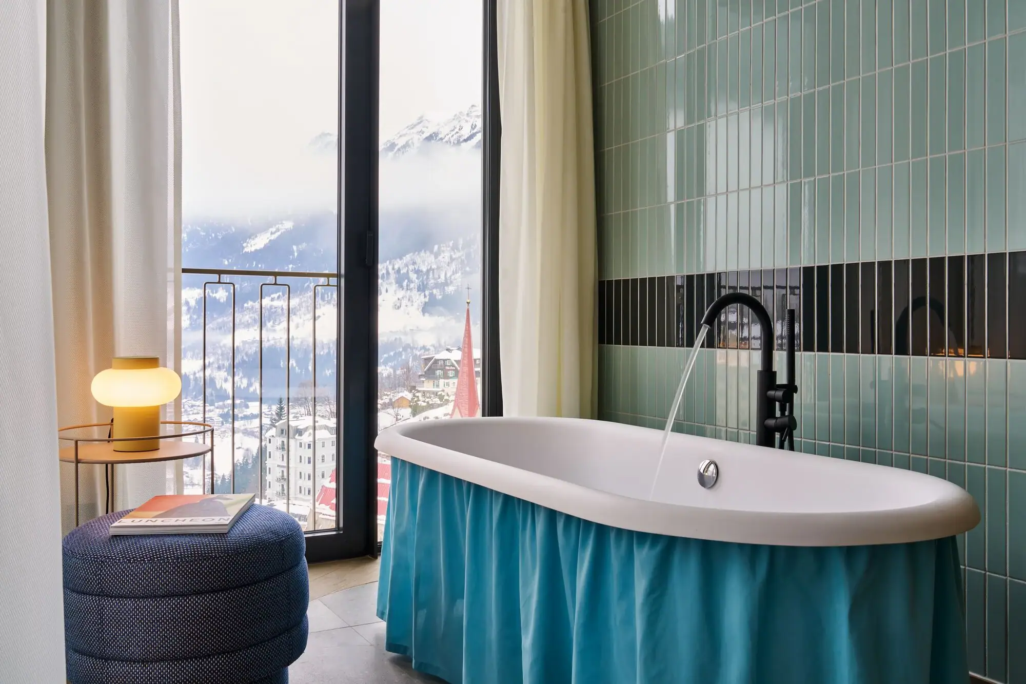 Bath A bath with a blue skirt in a bathroom with a window overlooking a snow-capped mountain range.