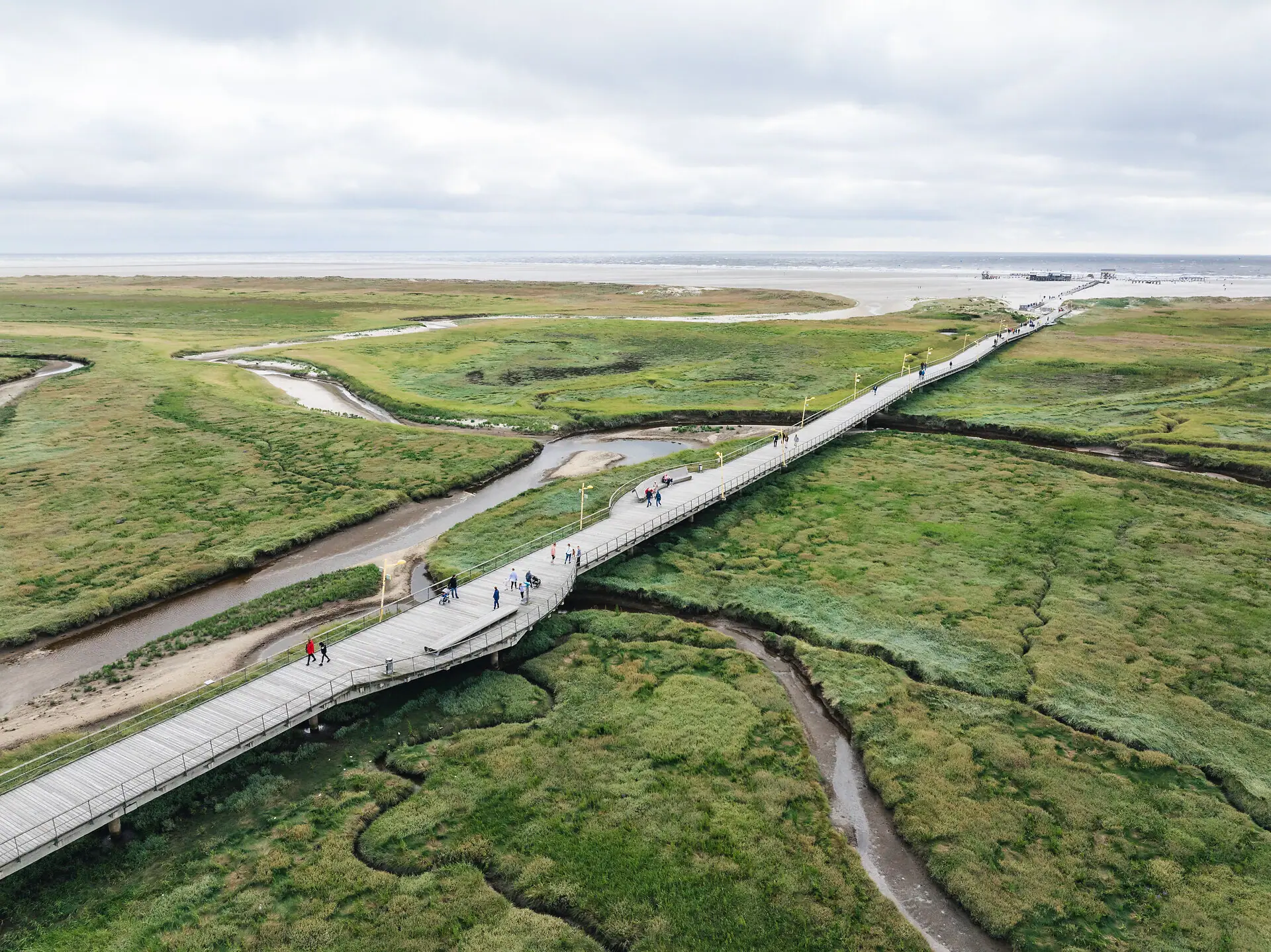 Dünenaufgang Brücke über ein sumpfiges Gebiet mit Gras und bewölktem Himmel.