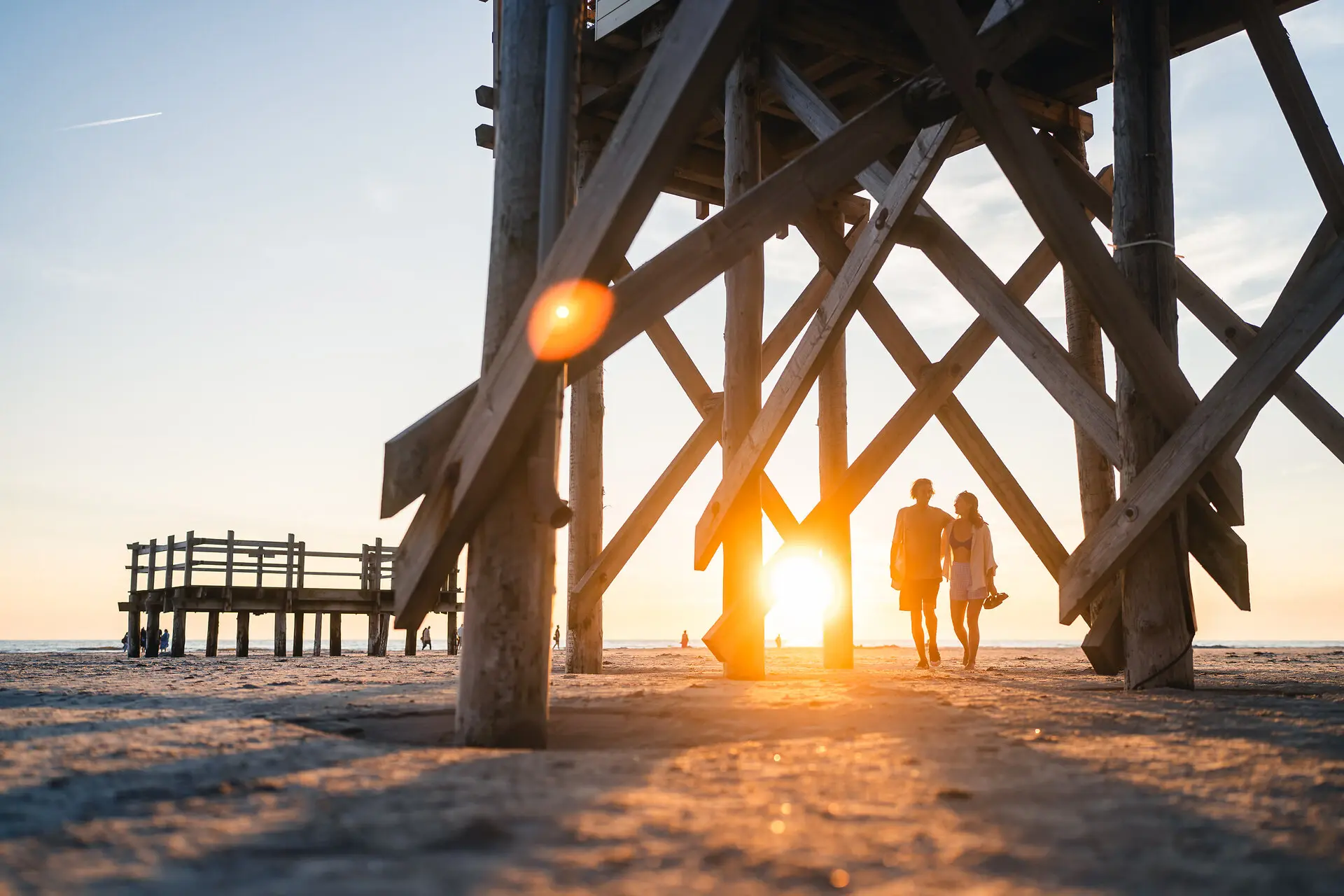 Beach A couple walks on the beach under a wooden structure.